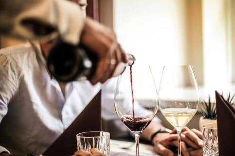 A man pouring wine into a glass at a restaurant table.